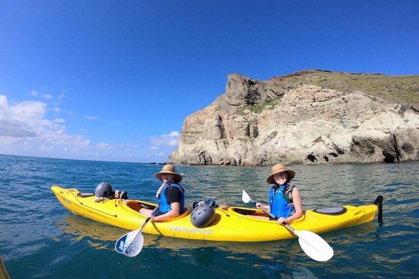 Two people kayaking on a calm sea with a rocky coastline in the background. 5