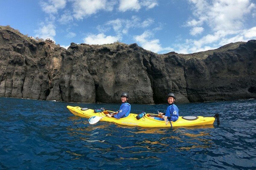Two people kayaking on a body of water with rocky cliffs in the background. 3