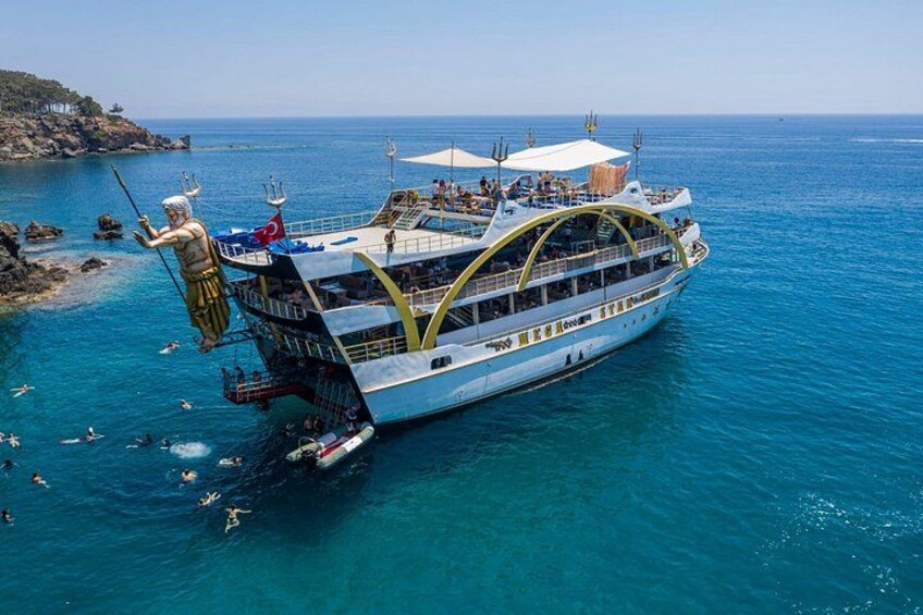 Ein großes Schiff mit einer Statue einer Figur auf dem Bug, umgeben von klarem, blauem Wasser und einer felsigen Küstenlinie. 1