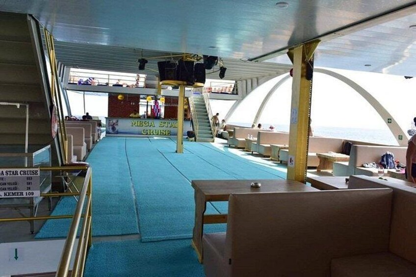 Innenansicht eines Kreuzfahrtschiffs mit blauem Teppichbereich, Sitzgelegenheiten und einer Bühne mit einer Werbetafel. 4