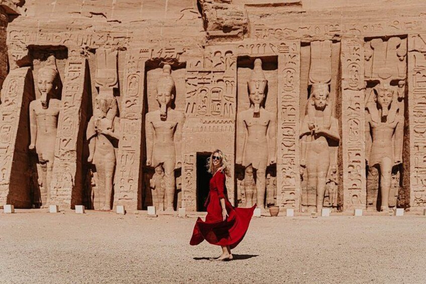 En person i en röd klänning som går förbi antika egyptiska statyer. 3