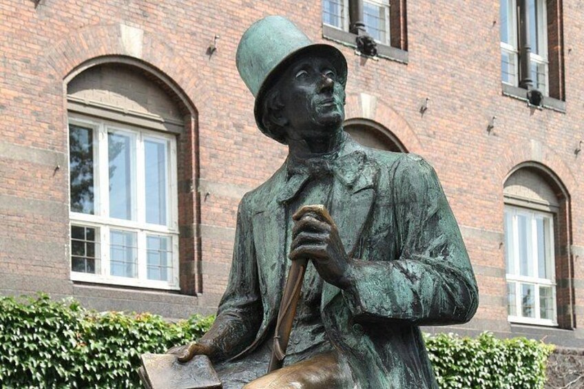 Una estatua de un hombre con traje y sombrero que sostiene un bastón, con un edificio de ladrillo y ventanas al fondo. 4