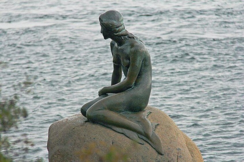 Una estatua de bronce de una figura sentada sobre una roca junto al agua. 3