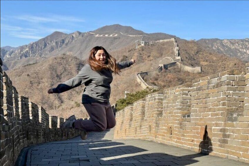 A person jumping on the Great Wall of China with mountains in the background. 3