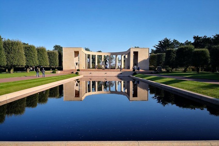 A modern building with a reflective pool in front, surrounded by neatly trimmed hedges and a clear blue sky. 4