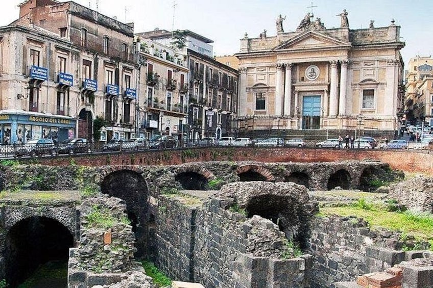 Des ruines antiques avec des arches, un bâtiment historique orné de statues et des véhicules modernes dans la rue. 1