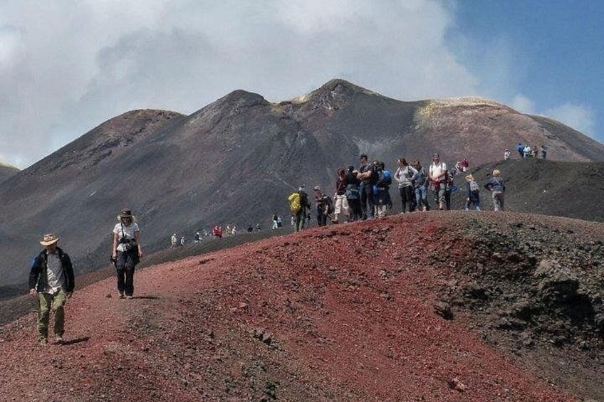 Un groupe de personnes fait de la randonnée sur une pente volcanique rouge, avec une montagne en arrière-plan. 3