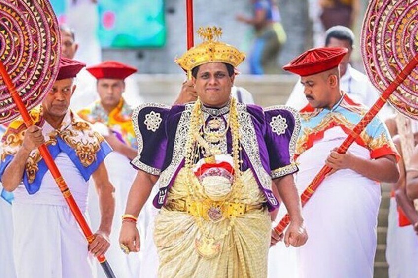 A person in elaborate traditional attire with a crown, holding a ceremonial staff. 1