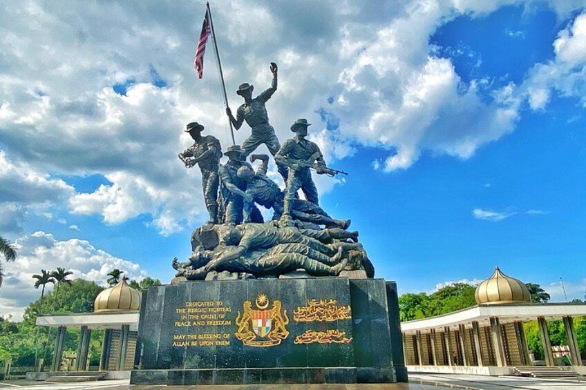 Una estatua de soldados con una bandera estadounidense, rodeada de follaje y un cielo despejado. 2
