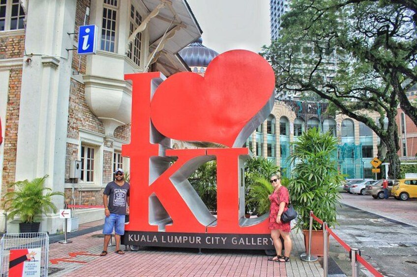 A large red 'K' and heart-shaped 'i' sign for Kuala Lumpur City Gallery, with a man and woman standing in front. 4
