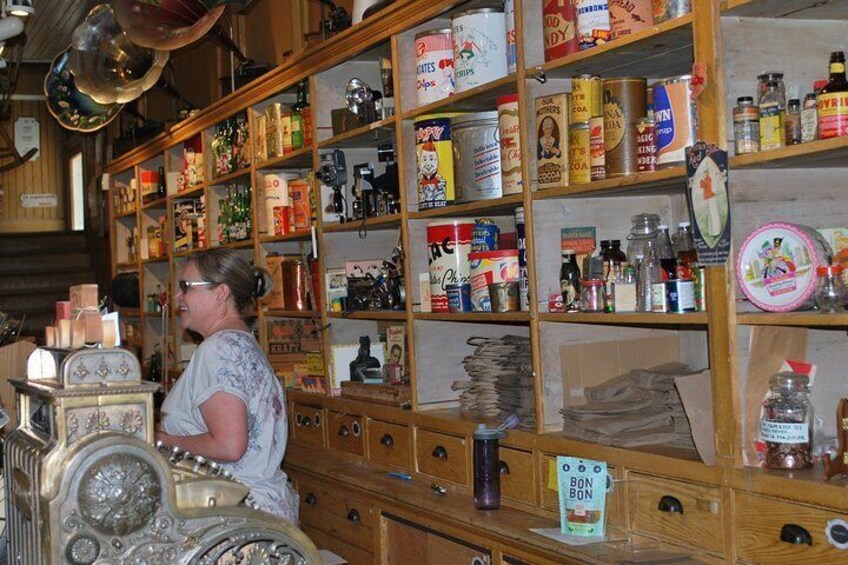 A woman in a vintage shop with shelves stocked with canned goods, jars, and other items. 2