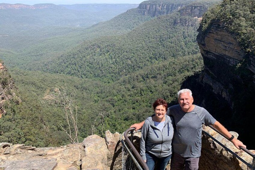 Una pareja de pie sobre un risco con vistas a un cañón con acantilados escarpados y un bosque denso. 2