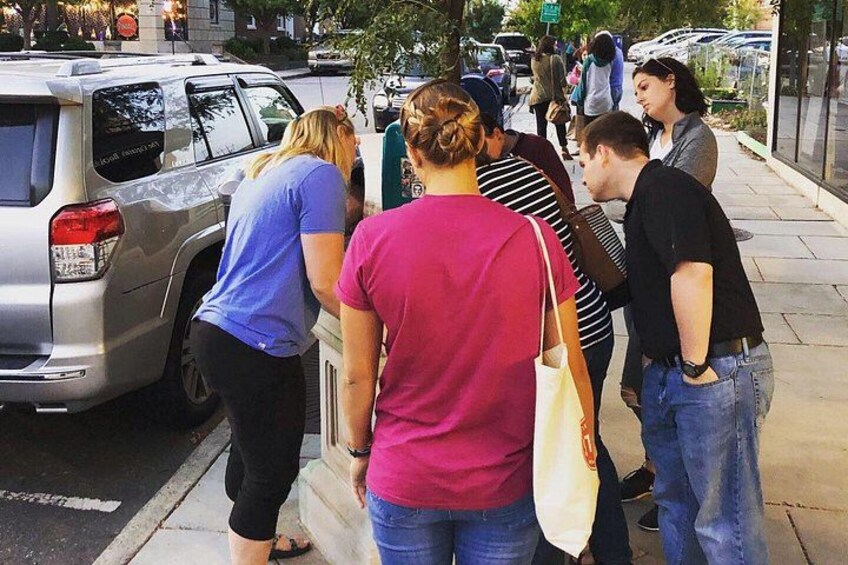 A group of people standing on a sidewalk, a parked car, and a street with a curb. 2