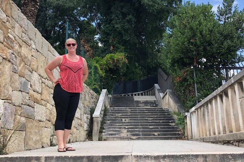 A woman standing on a stone staircase with a railing, surrounded by trees. 5