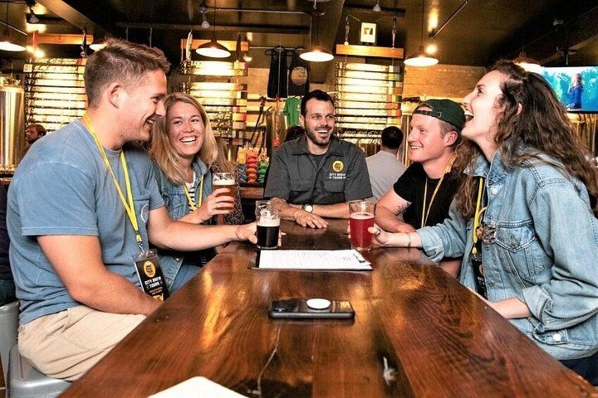Un groupe de personnes est assis autour d’une table en bois dans un bar, et elles tiennent chacune un verre à la main. 2