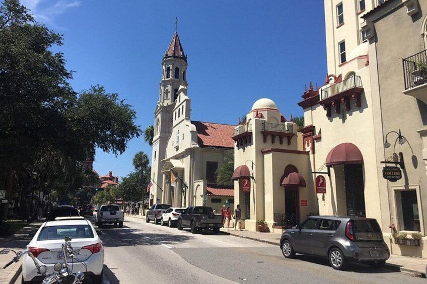 Una calle con autos estacionados, una iglesia con un campanario y un edificio con una cúpula. 1