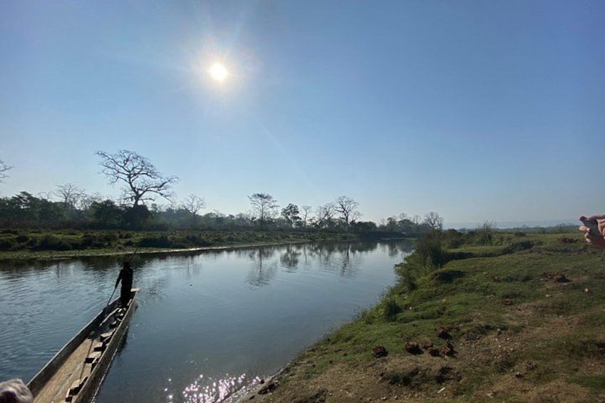 A calm river with a wooden boat docked on the left, surrounded by grassy banks and sparse trees under a clear sky. 3