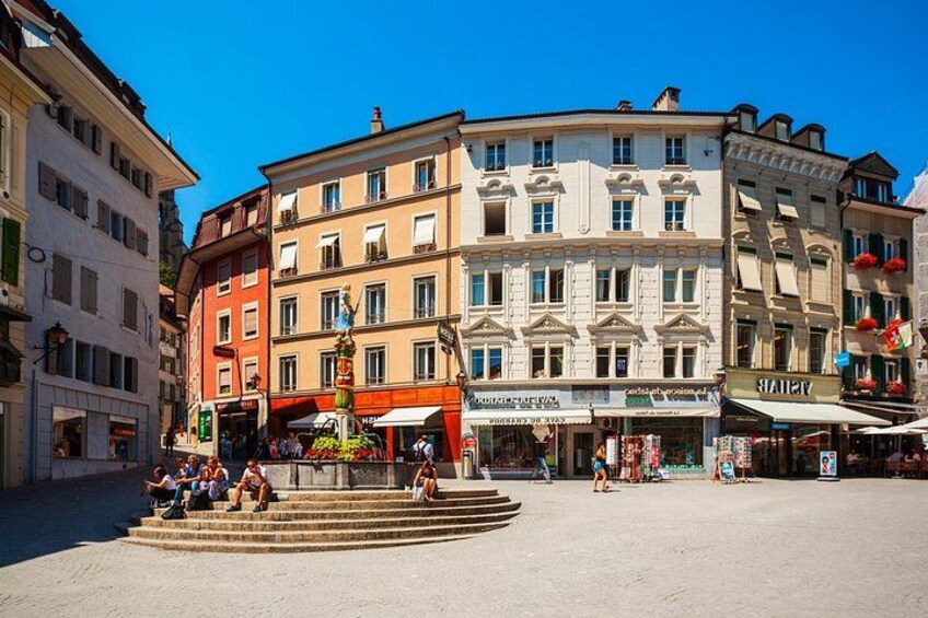 A square with buildings, a fountain, and people sitting and walking. 5