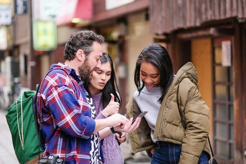 Three people standing on a street, one holding a smartphone. 2