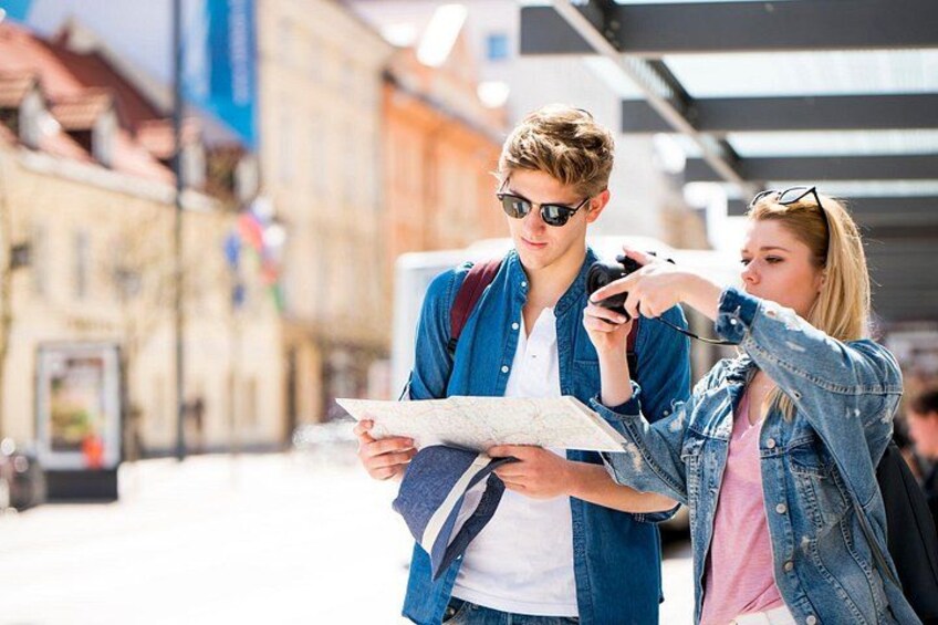 Two people examining a map in an urban setting with buildings and a clear sky. 3