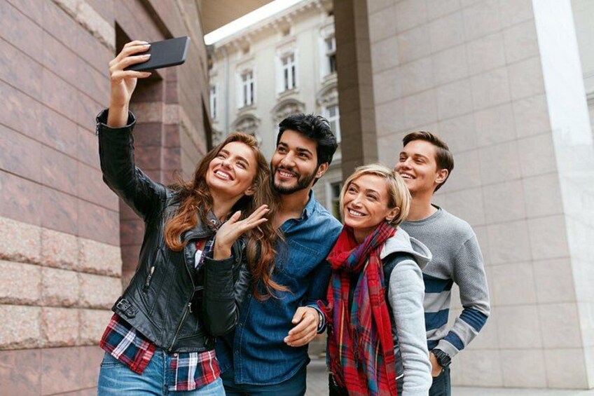 A group of people taking a selfie in an urban setting with classical architecture. 1
