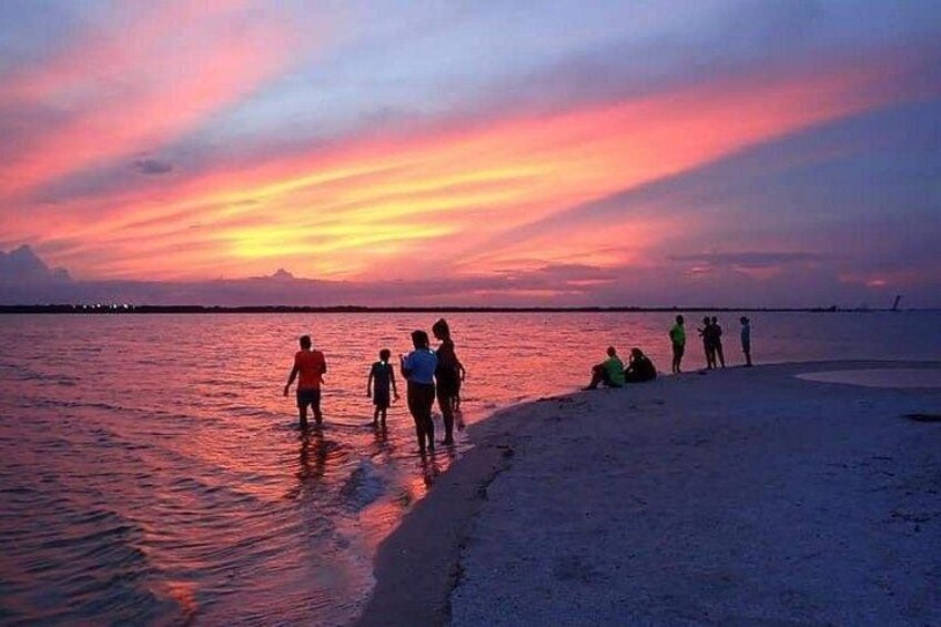 A sunset over a beach with people walking and sitting on the sand. 5