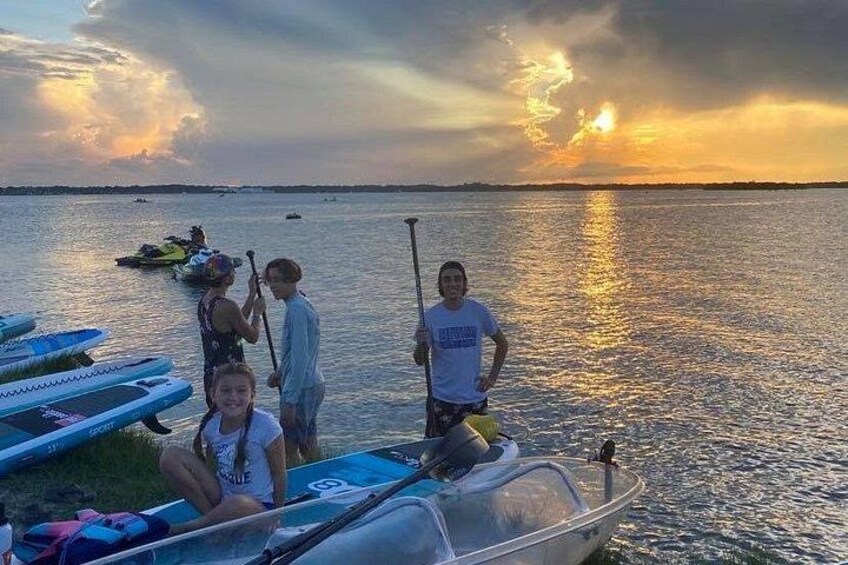 A sunset over a calm body of water with paddleboards and kayaks. 4