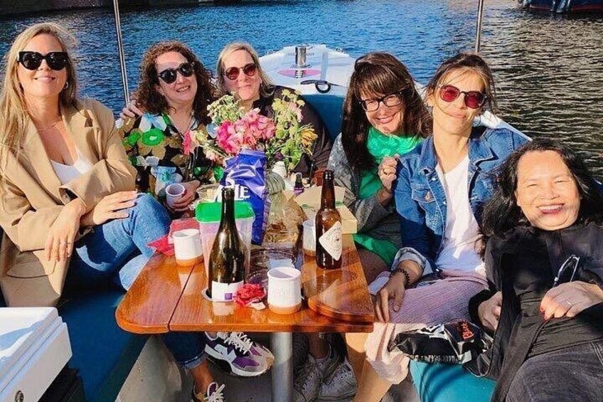 Un gruppo di persone su una barca con un tavolo apparecchiato con bottiglie e fiori. 2