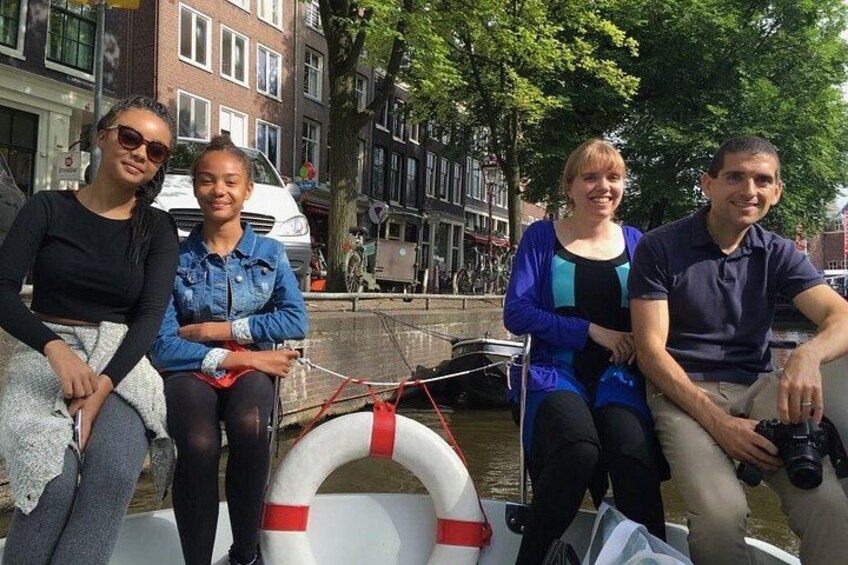 Quattro persone sedute su una barca in un canale, sullo sfondo edifici e alberi. 3