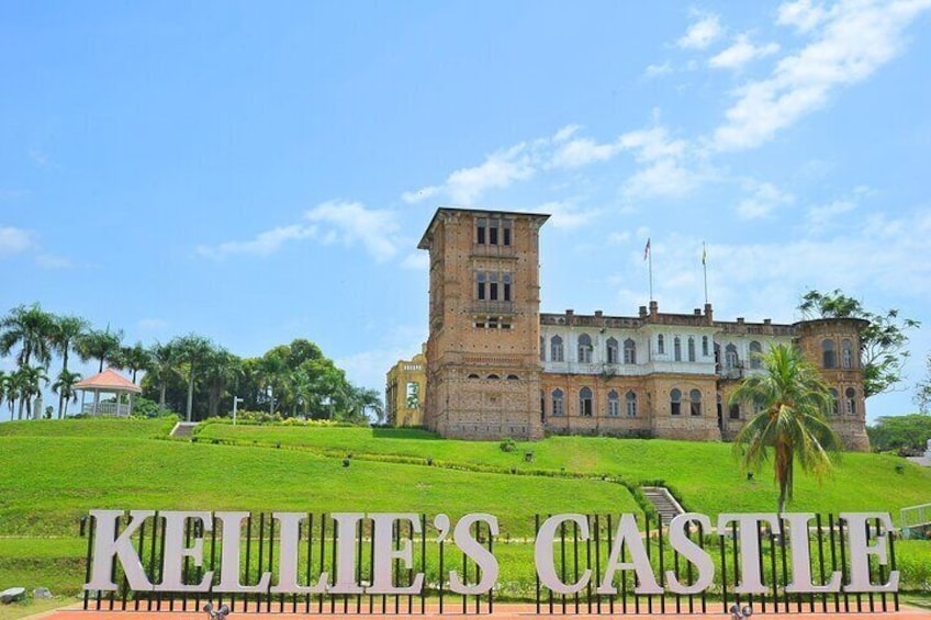 Kellie's Castle with a large tower, surrounded by a well-maintained lawn and palm trees. 1