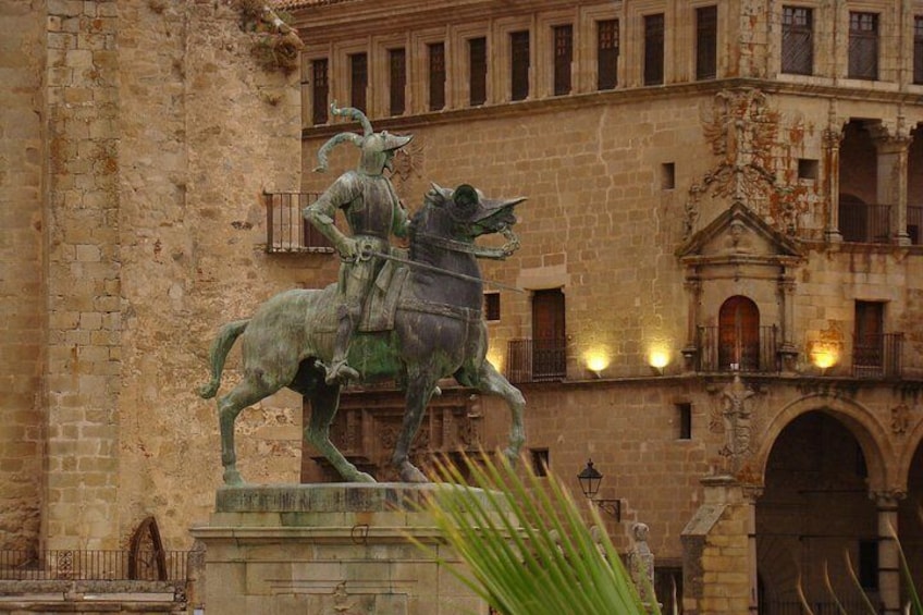 A statue of a knight on horseback in front of a historic building with balconies and arched doorways. 1