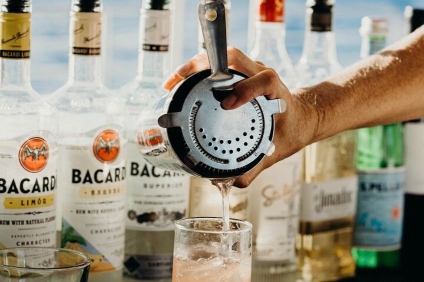 A hand squeezing a citrus juicer over a glass, with Bacardi bottles in the background. 3