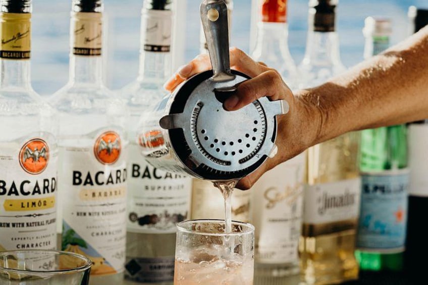 A hand squeezing a citrus juicer over a glass, with Bacardi bottles in the background. 2
