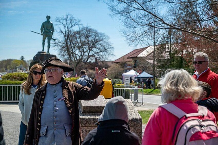 A statue of a figure on a pedestal, people standing and walking around, and a clear blue sky. 2