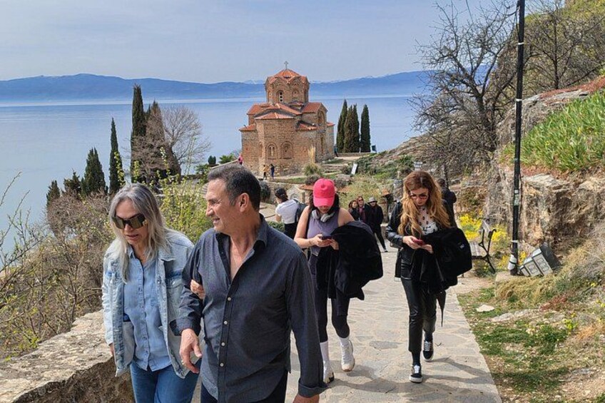 A group of people walking on a stone pathway by a body of water with a church in the background. 2