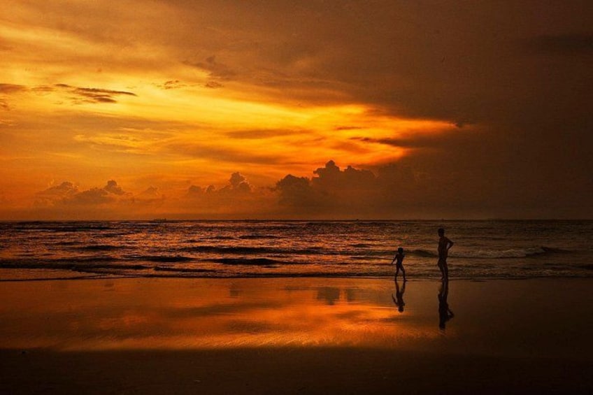 A sunset over a beach with two people walking. 2