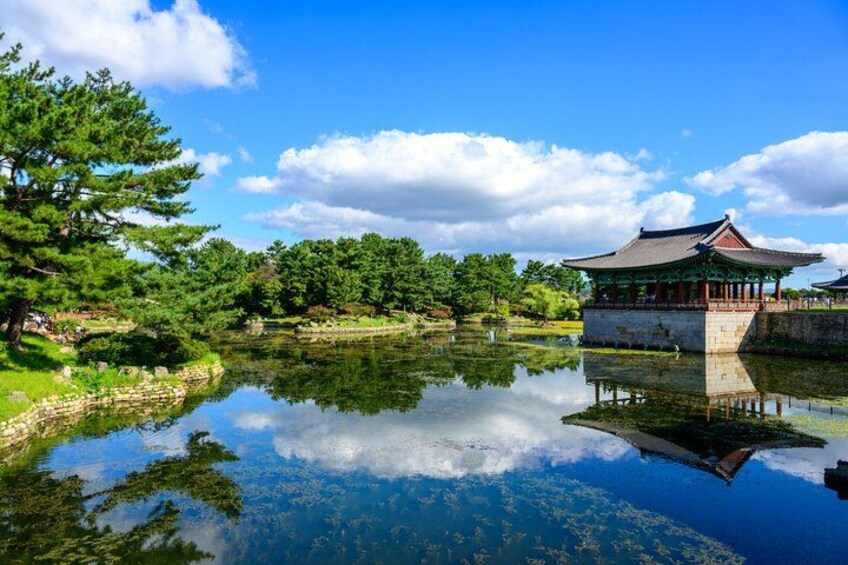 A traditional Korean pavilion by a calm pond with lush greenery and a clear blue sky. 2