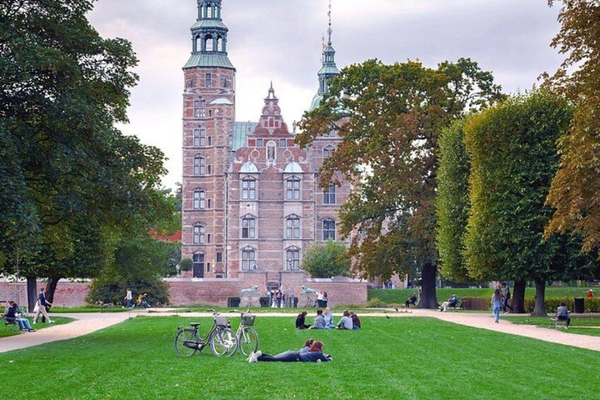 A large historic building with a tower, surrounded by a well-maintained park with grass, trees, and people. 5