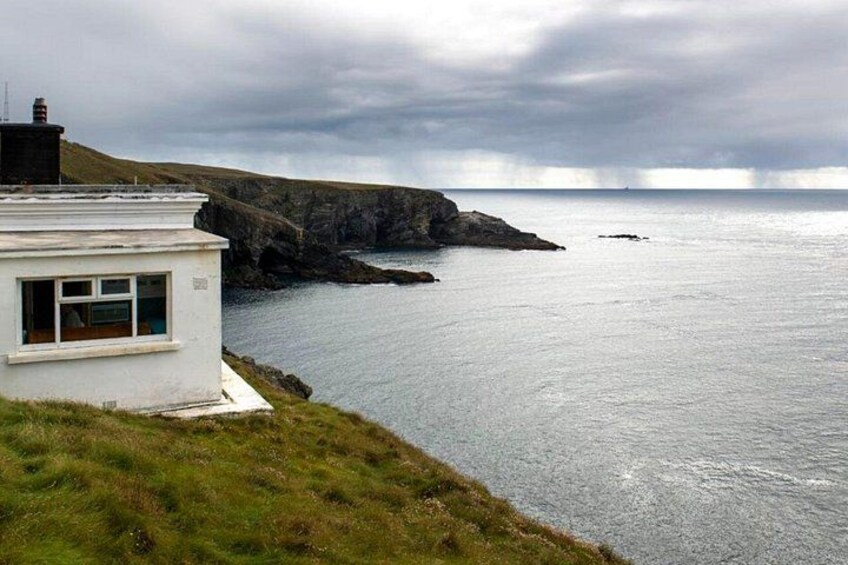 A coastal landscape with a white building, rocky cliffs, and calm sea. 2