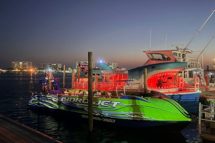 A green speedboat docked at a pier with city lights in the background. 3