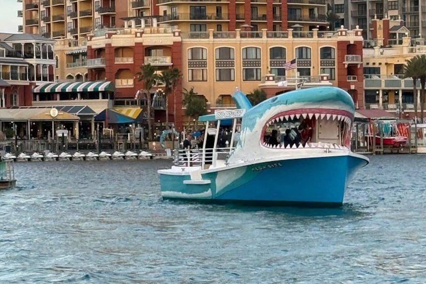 A blue boat with a shark mouth design on the front, sailing on a body of water with buildings in the background. 4