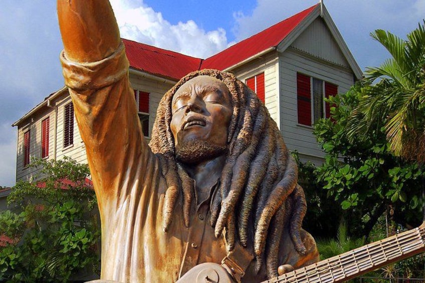 Una estatua con los brazos levantados, un edificio de techos rojos y abundante vegetación al fondo. 2