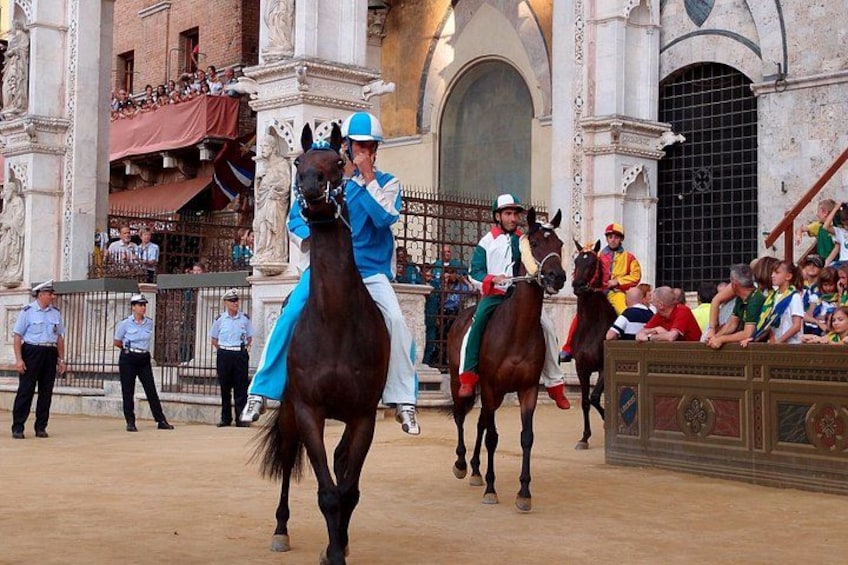 Un evento di equitazione con cavalieri in abiti colorati, spettatori e un edificio storico sullo sfondo. 1