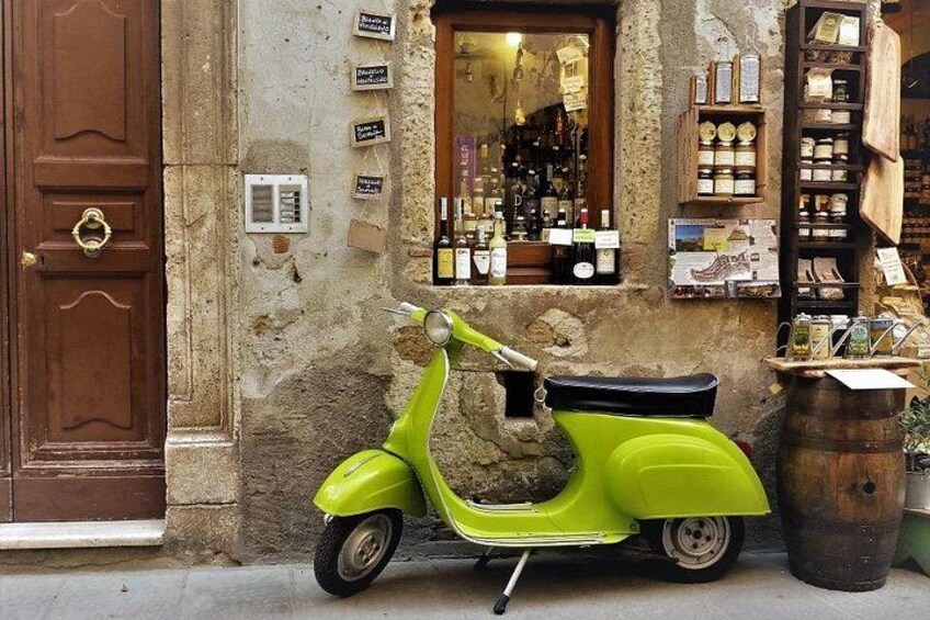 A green scooter parked on a cobblestone street next to a building with a wine shop. 2