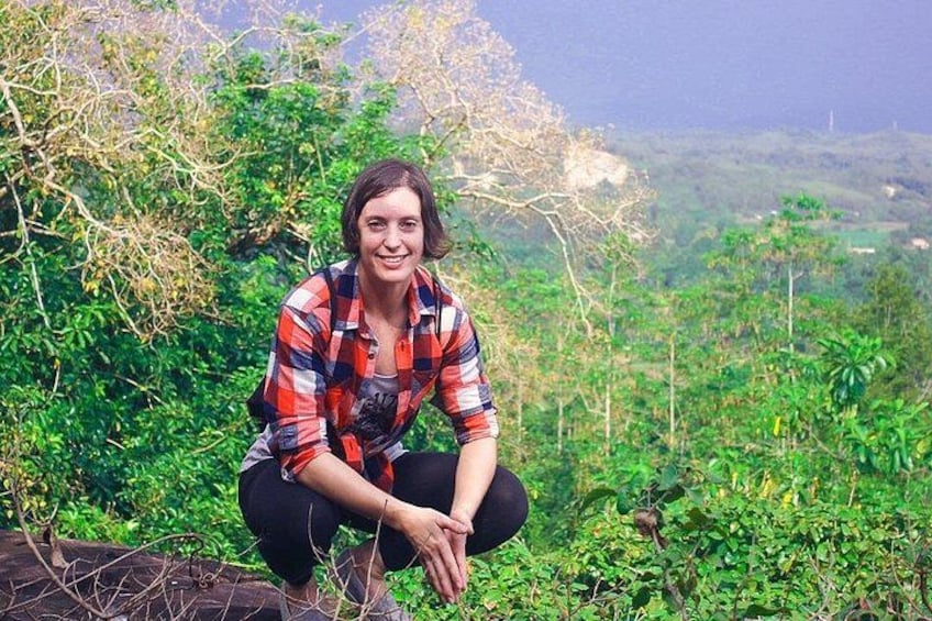 A person crouching in a natural setting with greenery and hills in the background. 2