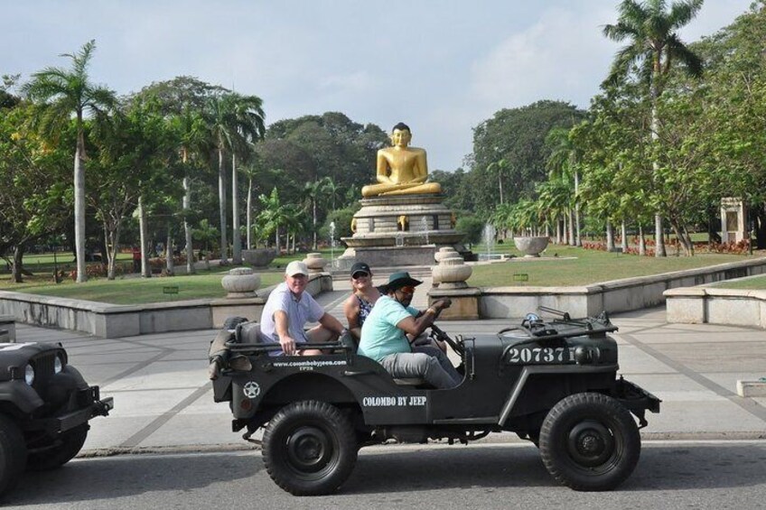 Un jeep negro con tres pasajeros pasando junto a una estatua dorada de Buda en un parque. 2