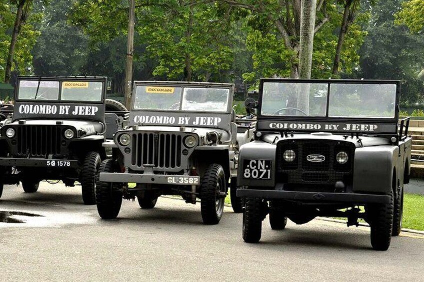 Tres jeeps militares negros con la inscripción 'Colombo by Jeep' en el frente, estacionados en una carretera con árboles al fondo. 1