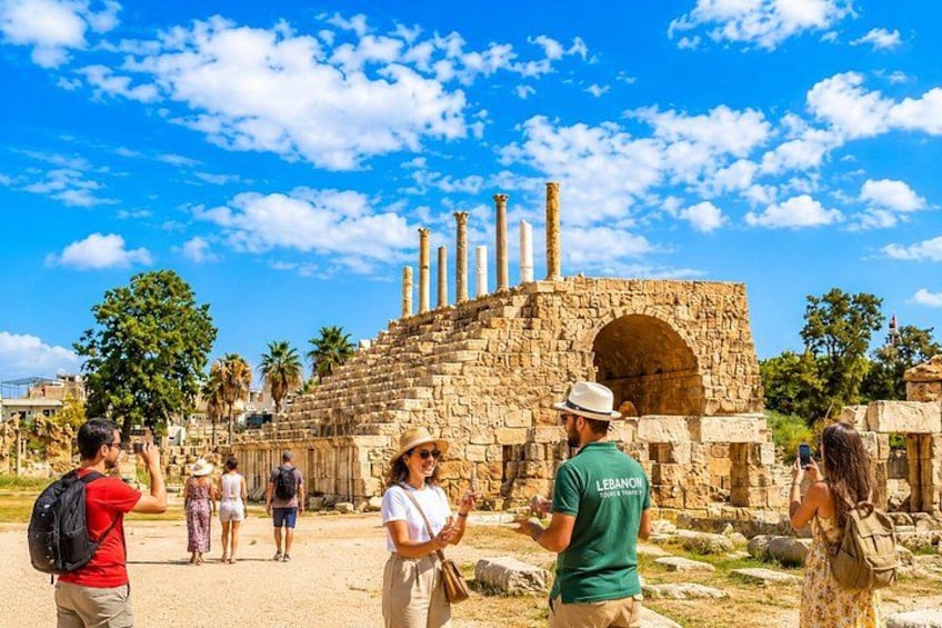 Ancient ruins with columns and an arched entrance, surrounded by tourists. 1
