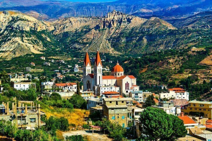 A mountainous town with a prominent church featuring two towers and a dome, surrounded by residential buildings and greenery. 1