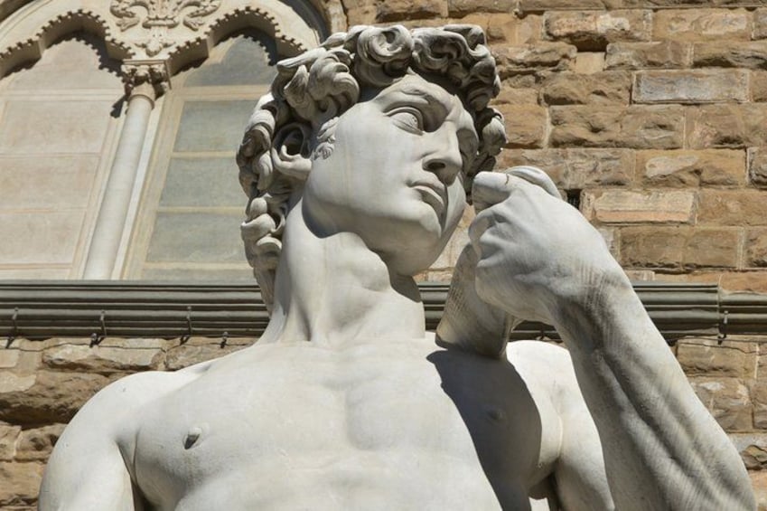 A classical statue with a draped garment, set against a stone wall with a window. 2